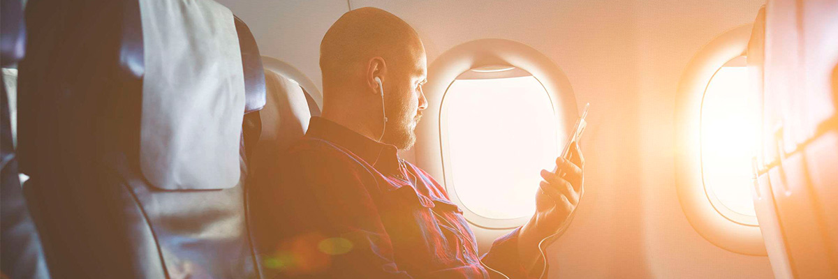 Young man listening to music and looking out the window, while is sitting in plane.